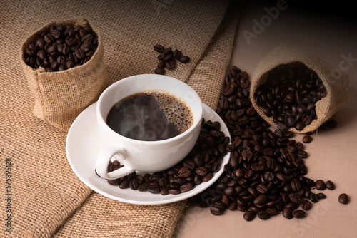 Hot coffee in a white cup of coffee and many coffee beans lying around