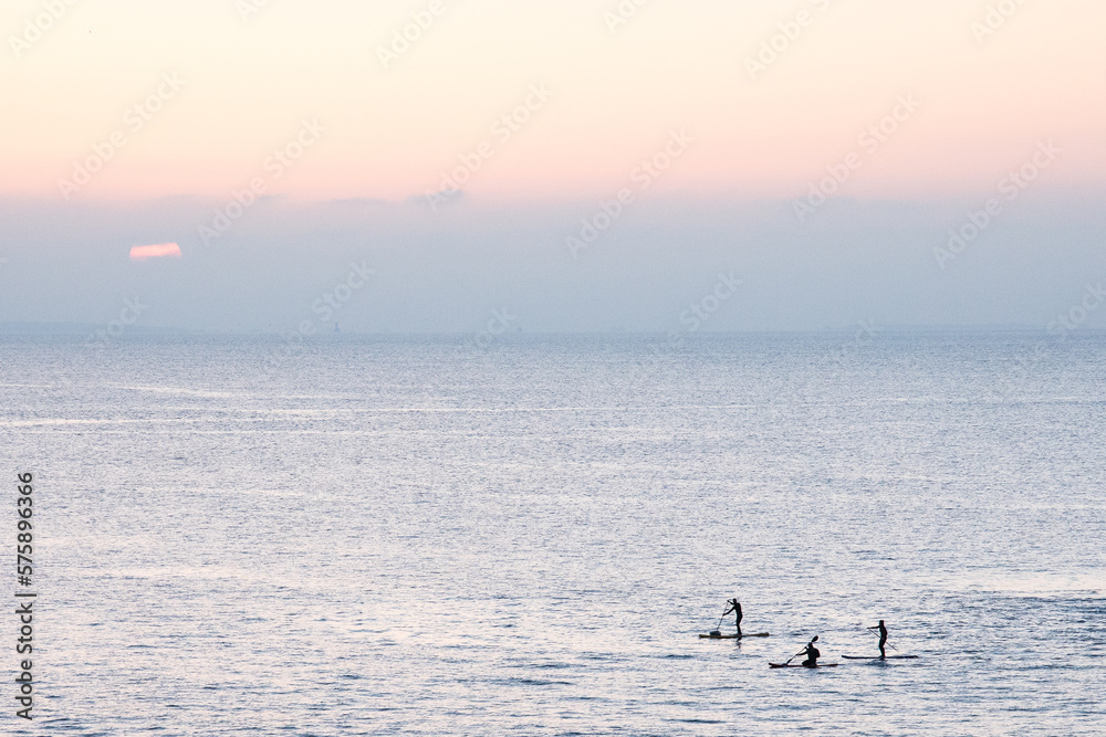Photographie de paddles sur l'océan au soleil couchant.