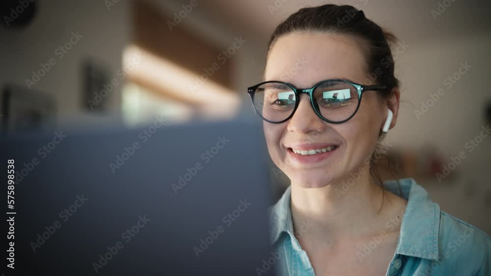 Portrait of a young adult caucasian woman wearing glasses taking a video call on a laptop.