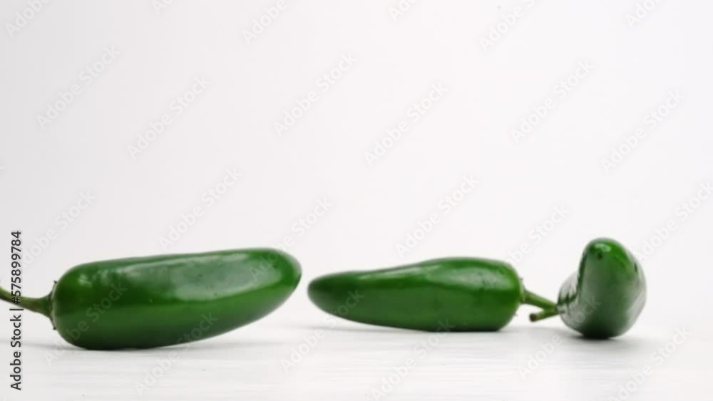 Whole green jalapeños falling and bouncing on white studio backdrop in