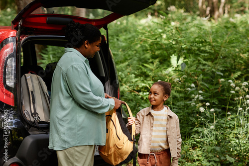 Side view portrait of African American mother and daughter standing by car in nature trail