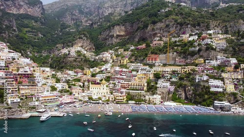 Aerial drone footage of the Marina Grande beach, chiesa (church) of Santa Maria Assunta in Positano, Amalfi coast, Campania, Italy. Establish scene of parasol, sun loungers, people swimming from above