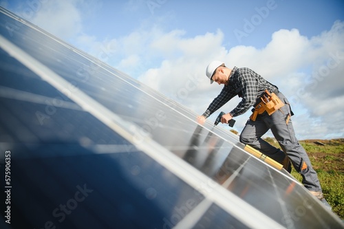 Male worker in uniform outdoors with solar batteries at sunny day. © Serhii