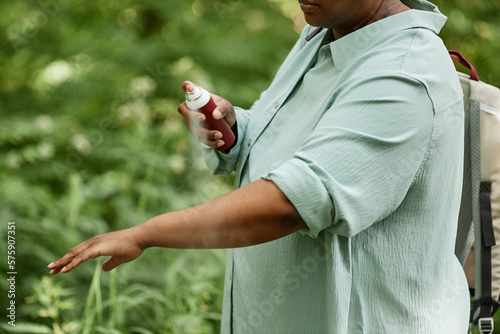 Side view closeup of black woman spraying arms with bug repellent outdoors in nature, copy space  photo