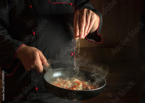 Fototapeta Naklejka Na Ścianę i Meble -  Cooking fresh vegetables. The cook adds salt to a steaming hot pan. The idea of European cuisine for a hotel with advertising space.
