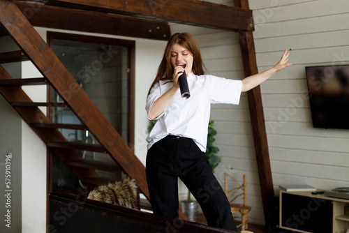 A young housewife sings and dances on a sofa in a home interior.