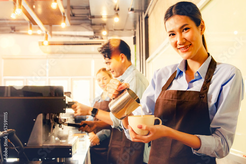 Beautiful asian barista pours milk froth into latte art coffee cup to decorate beauty appetizing aromatic and mellow together with the barista staff making customer service in a vintagen style cafe. photo