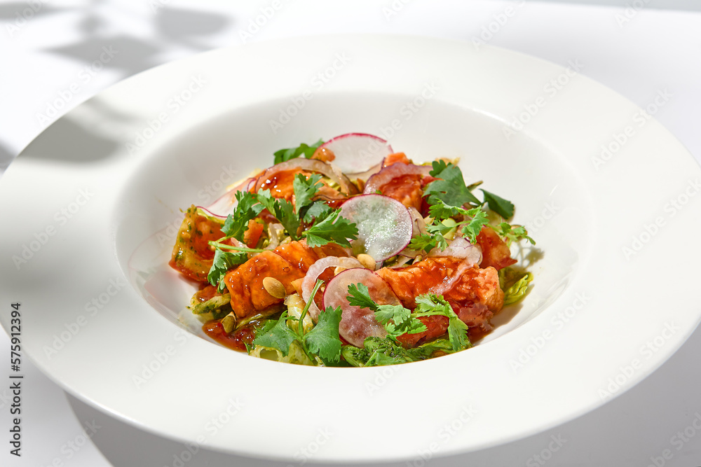 Elegant salad with baked salmon in sauce with vegetables on white table with harsh shadows. Salmon salad with radish on white background with shadows of leaves. Summer salad with roasted trout.