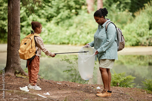 Leinwand Poster Side view portrait of black mother and daughter helping cleaning nature together