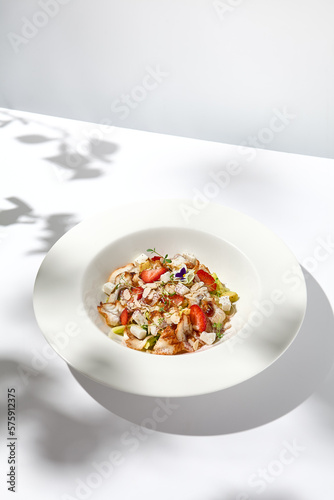 Elegant salad with smoked eel, strawberry and avocado on white table with harsh shadows. Eel salad with berries on white background with shadows of leaves. Romantic dining with fish appetizer.