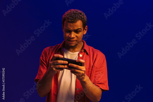 African man frowning while playing online game on mobile phone isolated