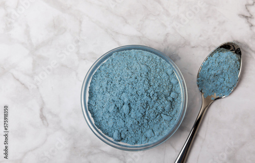 Blue spirulina powder in bowls and spoons on a marble table. Natural vegan superfood. Healthy food supplement. Phycocyanin extract. Place for text. Place for a copy. photo