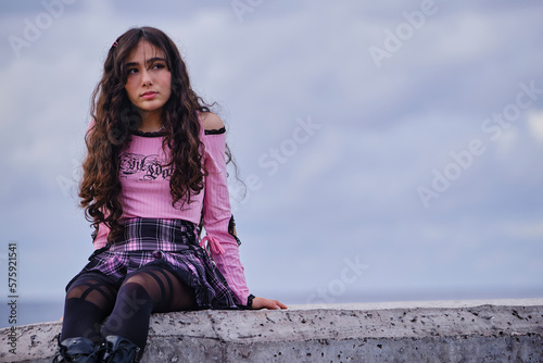 Portrait of smiling teenage girl with gothic and boyish look posing sitting on a wall in front of the sea. 