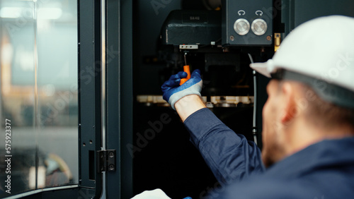 Back view of Caucasian production engineer in safety wear inspecting CNC machine to fix an error. A male factory worker is maintaining industrial machine that is used to control the production line.