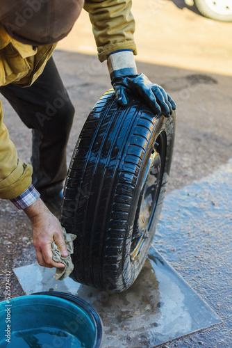 Outdoors, selective focus on a wheel from a passenger car, which a man in one glove washes with a rag with water from dirt and dust, carefully washing the cracks, copy space.