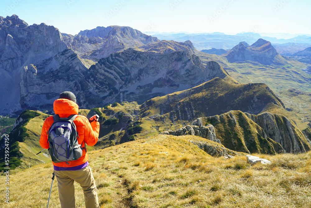 Photographed from the back, a male tourist stands against the background of picturesque slopes and beautiful peaks on a mountain path in the Durmitor National Park, Montenegro