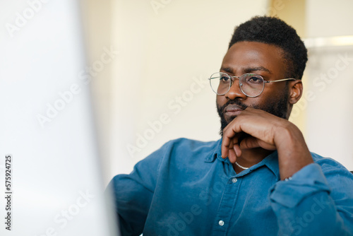 Black male entrepreneur working with computer in office, focused african american businessman looking at monitor screen
