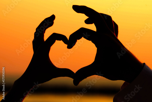 Silhouette of hands making hands as heart shape with beautiful sky in warm color twilight sunset background, heart,love and romantic concept. St Valentine's Day
