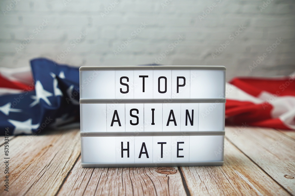 Stop Asian Hate word in lightbox and American flag on wooden background
