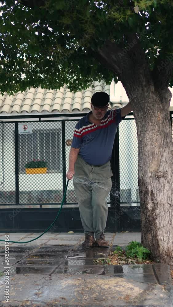 Retired man whistling while watering tree at the front of his home Retired man whistling while watering tree at the front of his home