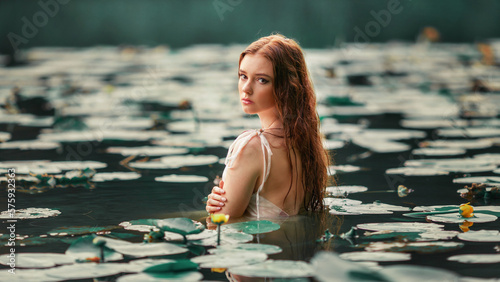 Beautiful red haired girl in white dress posing in river with water lilies. Fairytale story about  ophelia .Warm art work. photo