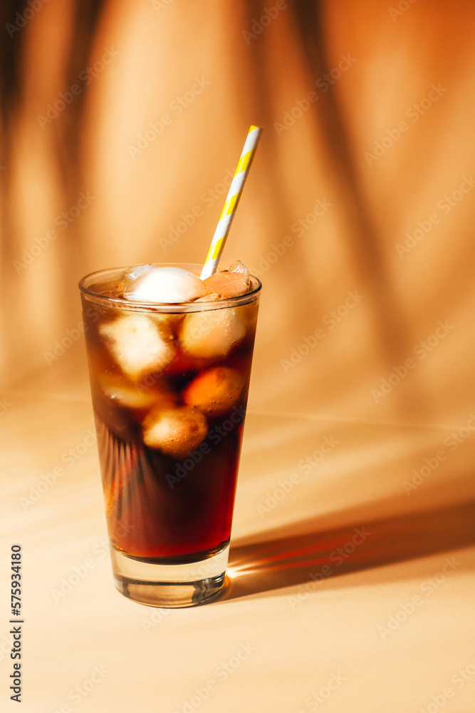 close-up on a glass with cola and ice on a beige background with shadows close-up on a glass with cola and ice on a beige background with shadows