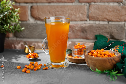 Orange tea on transparent cup. Homemade tea with sea-buckthorn isolation on concrete background. Vitamin tea with berries and citrus on upright glass on stone backdrop photo