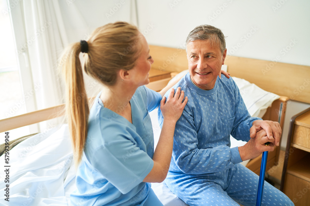 Fototapeta premium Caring nurse sitting with elderly man on bed at rehabilitation center
