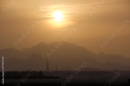 Sunset landscape with dark mountain peaks in egyptian desert and high voltage power lines