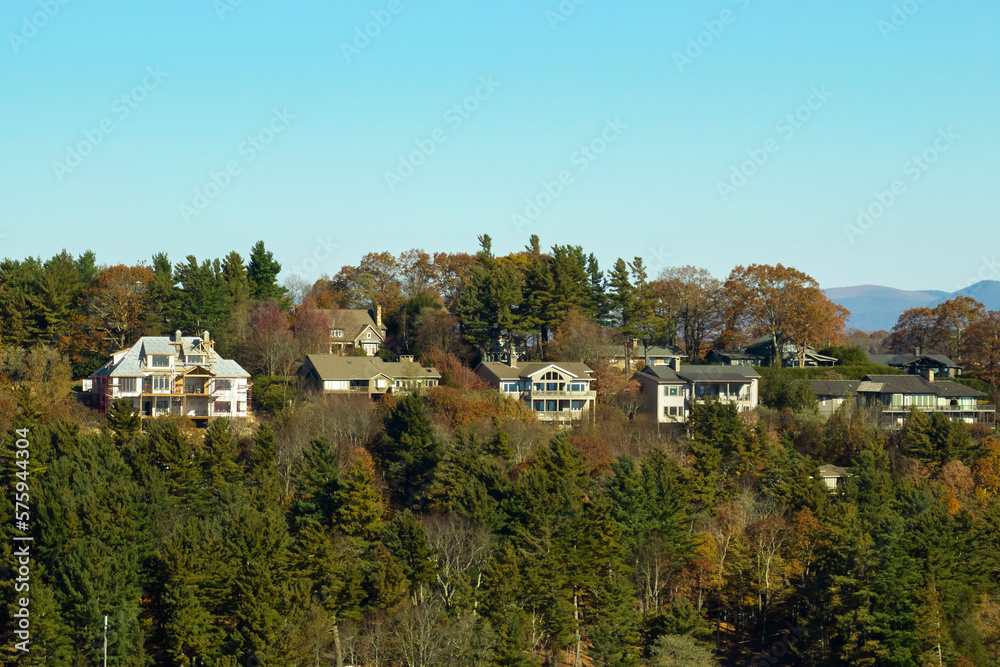 View from above of expensive residential houses high on hill top between yellow fall trees in suburban area in North Carolina. American dream homes as example of real estate development in US suburbs