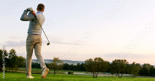 Handsome Caucasian golf player getting ready and hitting a ball with a club on a summer weather day. Outdoor. Golf field.