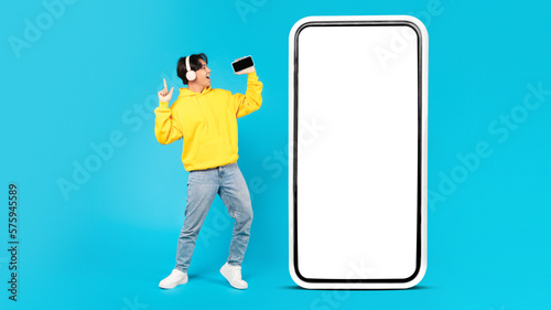 Asian Teen Guy Near Huge Phone Singing On Blue Background