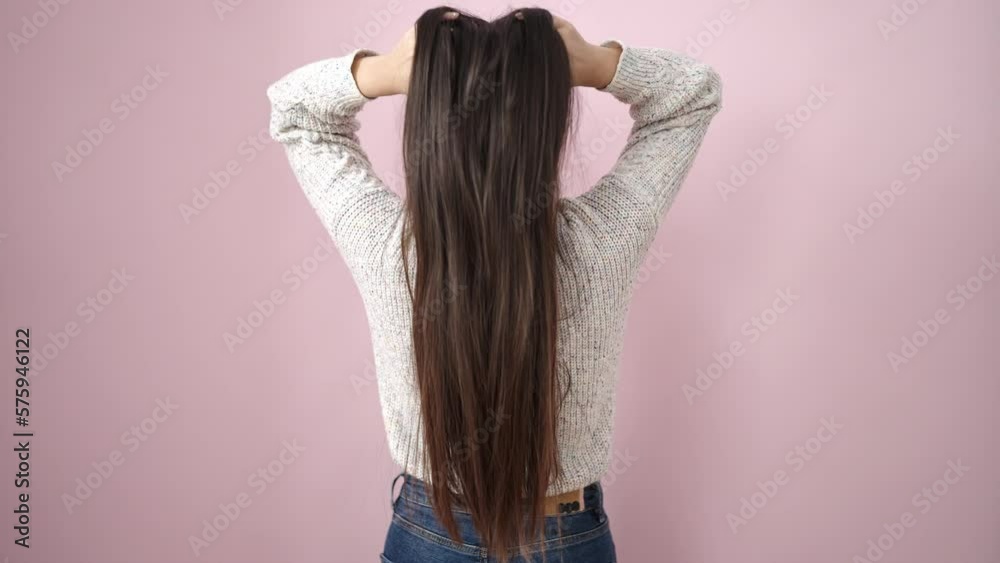 Young chinese woman combing hair with hands over isolated pink background
