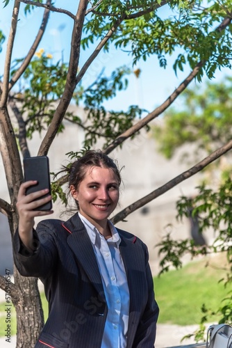 Executive woman smiling while taking selfies with her mobile phone outdoors.