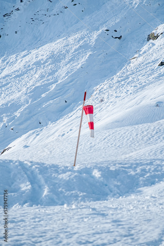 Red and white wind flag immersed in the snow of the mountain © Marco Bonomo