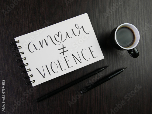 AMOUR ≠ VIOLENCE lettrage dans cahier avec tasse d'espresso et stylos sur bureau noir
