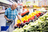 Elderly retired man buying eggplants in grocery section of the supermarket