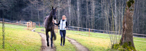 Young woman brings her horse on the bridle from the pasture to the stable, narrow cut motif half left.. photo