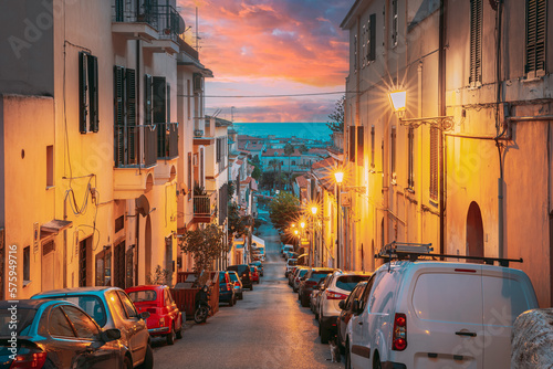 Fototapeta Naklejka Na Ścianę i Meble -  Terracina, Italy. Cars Parked On Narrowm Street In European City In Summer Night. Amazing Sunset Sky With Saturated Colorful Clouds. Scenic View. Travel Italy.