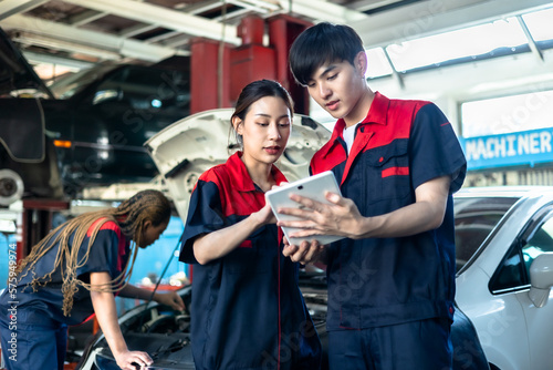 Asian automotive engineer people wear helmet work in mechanics garage.young auto mechanic in uniform is looking at camera and smiling examining car.