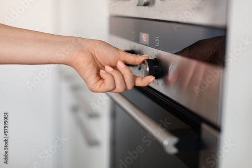 Unrecognizable Woman Turning Knob On Modern Oven In Kitchen