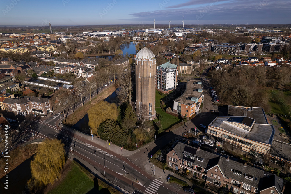 Cityscape of Zutphen with former Dutch brick water tower in now repurposed as a residential home in the foreground Hanseatic town in the background against a blue sky. 