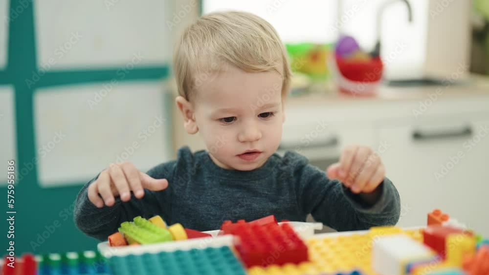 Adorable blond toddler playing with construction blocks sitting on table at kindergarten Adorable blond toddler playing with construction blocks sitting on table at kindergarten