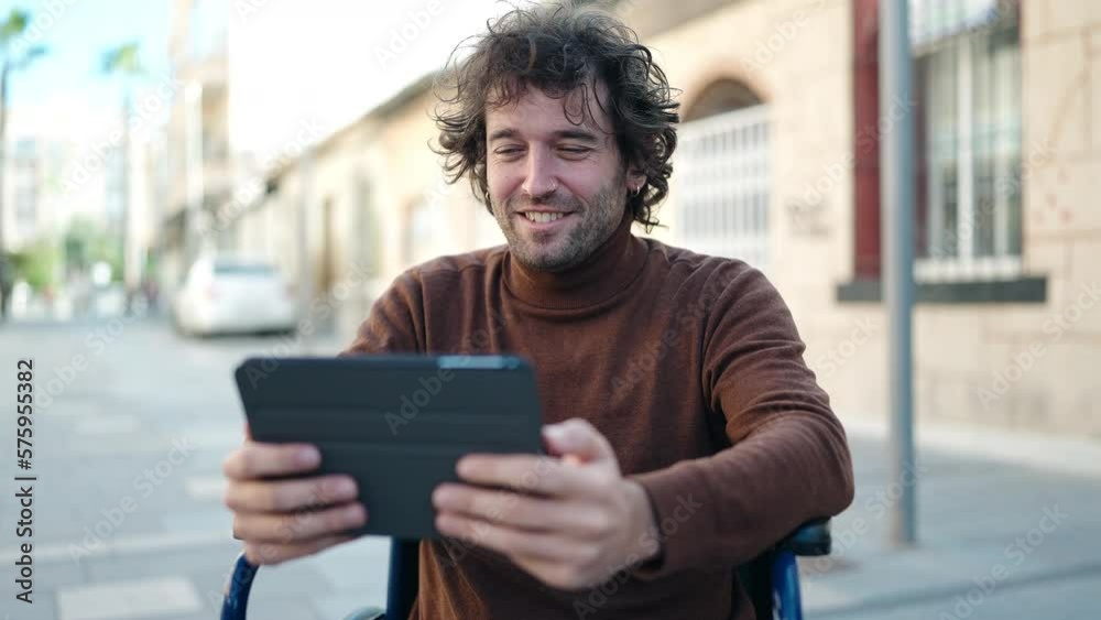 Young hispanic man using touchpad sitting on wheelchair at street Young hispanic man using touchpad sitting on wheelchair at street