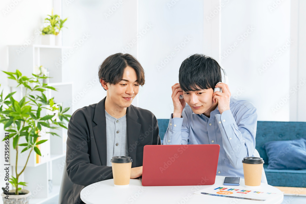 ノートパソコンを見る二人の若い男性 ノートパソコンを見る二人の若い男性