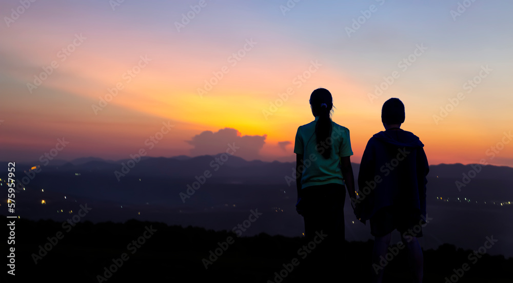 the back silhouette of a girl and a boy standing and watching the sunset