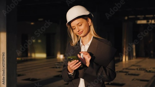 Portrait of Attractive Female Building Architect at Modern Unfinished Business Center Woman Texting by Smartphone and Smiles photo