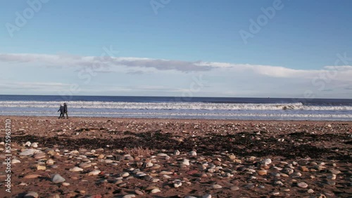 Drone flies very low, sideways over beach as people walk past. County Durham, England  photo