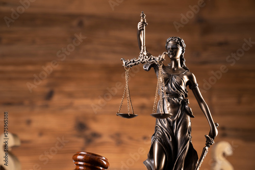 Law concept. Judge chamber. Judge’s gavel, Themis sculpture, scale and legal code on the shining brown desk. Brown background.