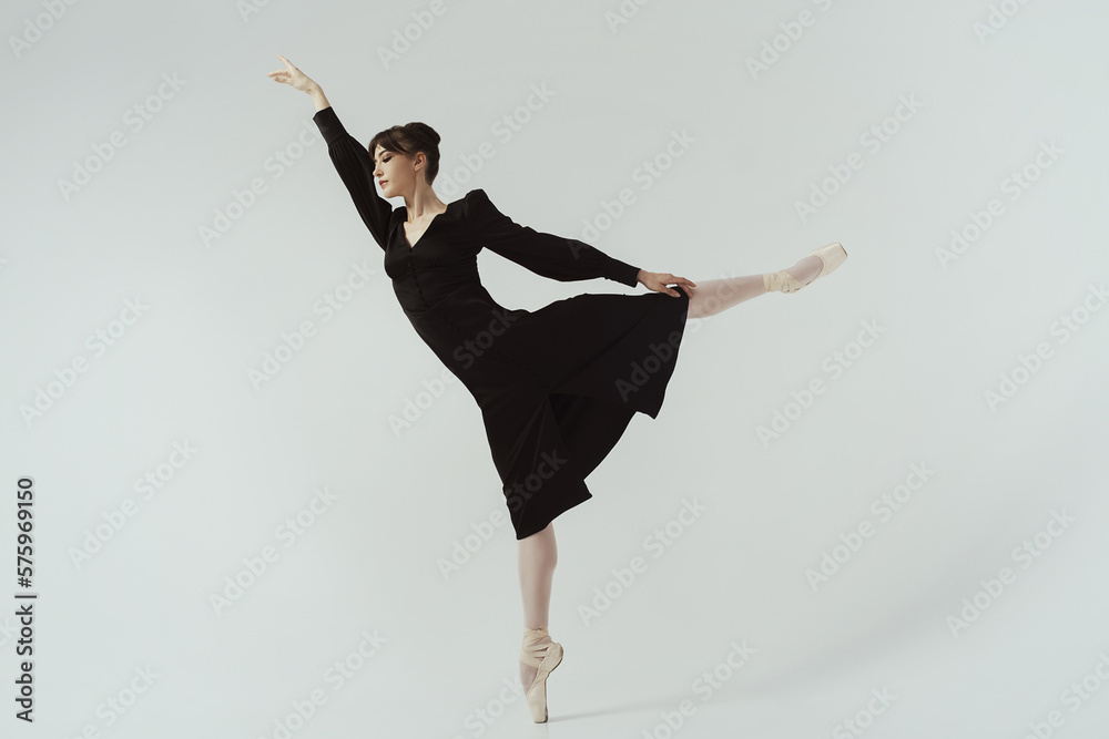 ballerina in a black dress and ballet shoes poses in a photo studio in